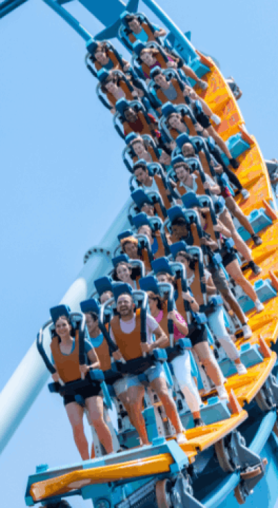 Riders on Pipeline: The Surf Coaster winding through a tight orange-track turn against a blue sky at SeaWorld Orlando