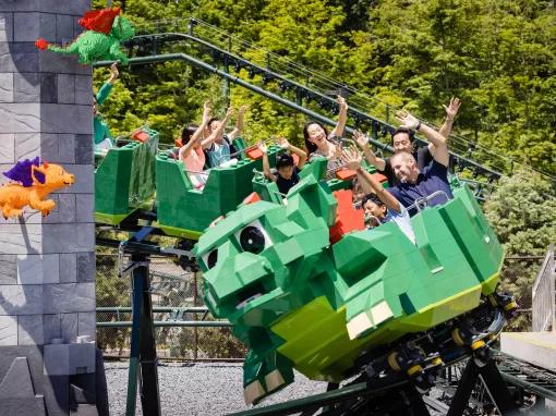 Adults and children smiling riding The Dragon with their arms in the air at LEGOLAND® New York Resort