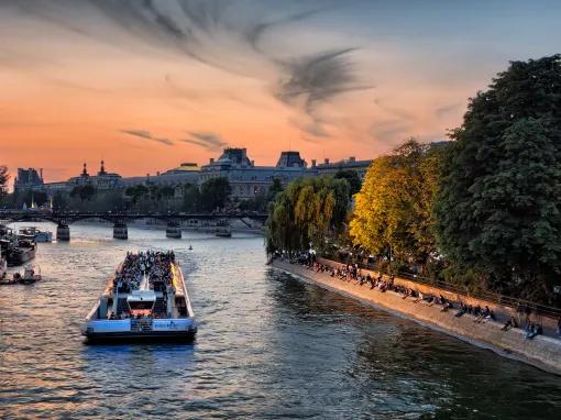A boat going down the Seine with building and trees on either side of the river