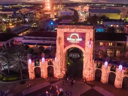 Bird’s eye nighttime view of Universal Studios Florida arches with a circular Halloween Horror Nights banner in the middle and the park illuminated behind.