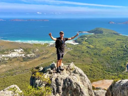 Happy man with arms raised, standing on a rock overlooking scenic views at Wilsons Promontory