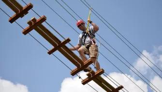 Man traversing swinging bridge on the Sceamin Gator Zip Line course at Gatorland in Florida