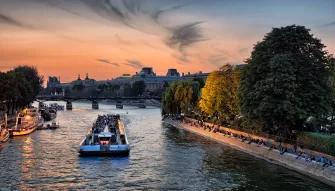 A boat going down the Seine with building and trees on either side of the river