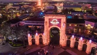 Bird’s eye nighttime view of Universal Studios Florida arches with a circular Halloween Horror Nights banner in the middle and the park illuminated behind.