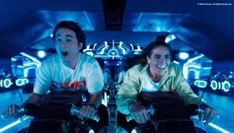 TRON Lightcycle/Run at Magic Kingdom Park Two young adults sat on motorcycles shaped vehicles TRON Lightcycle. They are leaning forward gasping with shock.