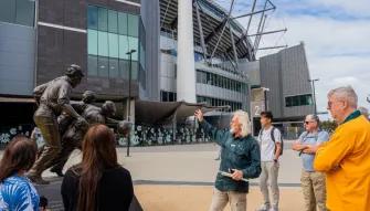 Tour guide showing a statue to a group of guests at the MCG Forecourt during the Melbourne City Discovery Tour