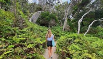 Woman walking toward Tidal River surrounded by natural bushland at Wilsons Promontory