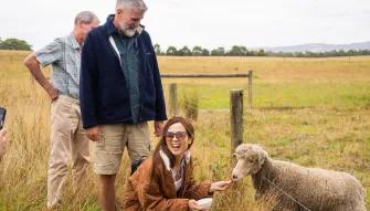 Woman smiling while feeding a sheep at Coldstream Dairy, with two other people watching in the background
