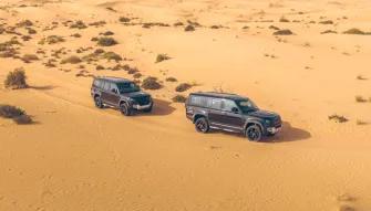 Two Land Rover Defenders driving through the Dubai desert