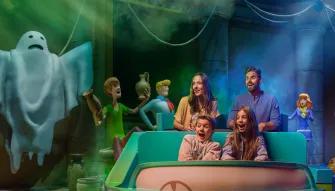 Warner Bros. World Abu Dhabi Guests enjoying the Scooby-Doo: The Museum of Mysteries ride at Warner Bros. World Abu Dhabi, laughing in a ride vehicle as a friendly ghost figure floats nearby.