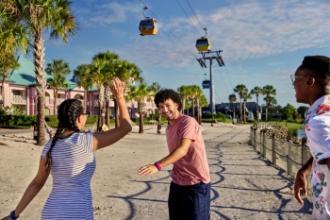 Friends standing on the beach of Disney’s Caribbean Beach Resort, laughing underneath the Skyliner