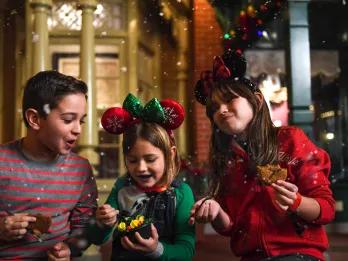 Two girls and a boy eating cookies and wearing Christmas jumpers