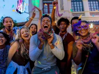 A group of friends in their twenties smiling and laughing at the camera, wearing lots of Mardi Gras beads