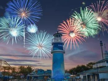 Multi-coloured fireworks being set off above a lighthouse as the sun is setting