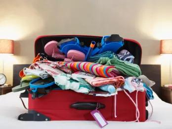 A red suitcase on top of a bed overflowing with clothes 