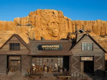 Uncharted at PortAventura World A wooden barn-like building in front of sandy cliffs with a carved Aztec face in the centre