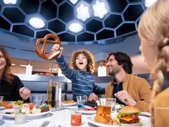 Dining at PYM Kitchen A child holding up a giant pretzel while sat at a table eating food with his two parents and sibling