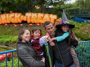 A family posing in front of a sign reading "Brick or Treat". The two children are dressed in Halloween costumes