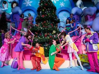 Christmas at Universal Orlando Resort Performers dressed as Whos from the Grinch wearing bright coloured clothes and exchanging gifts in front of a large Christmas tree