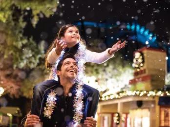 Christmas in Orlando A girl sitting on a man's shoulders holding her hands out to catch fake snow as it falls