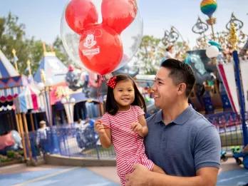 Kids Attractions at Disneyland Resort in California A man holding a young girl who is carrying a balloon standing in front of Dumbo the Flying Elephant