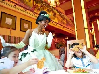 Tiana smiling with children sat at a table eating breakfast in Disneyland