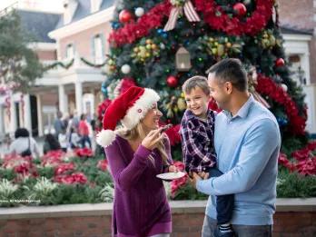 A man holding a small boy who is smiling at a woman eating a cookie and wearing a Santa hat