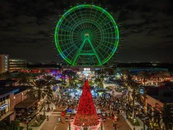 A view over ICON Park with a red Christmas tree in the foreground and The Wheel lit up green in the background