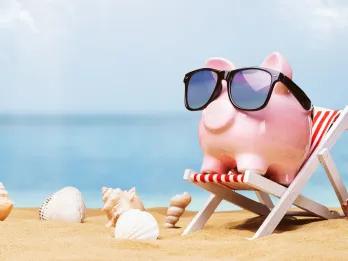 A pink piggy bank wearing sunglasses and sitting on a deck chair on a beach