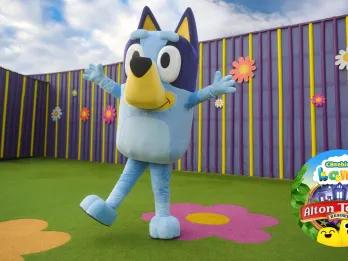 Bluey in Alton Towers Resort Big blue dog called Bluey with arms extended open and the Alton Towers CBeebies Land logo in the bottom right corner