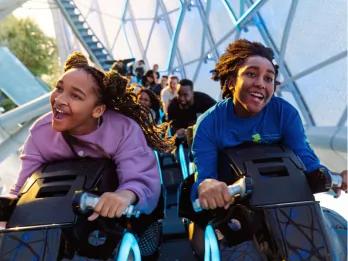 Guests riding TRON Lightcycle/Run Two guests smiling as they are launched, sat on bike shaped vehicle riding TRON Lightcycle/Run