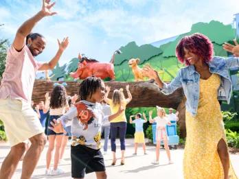 A man and woman dancing with a child in front of a Lion King themed building