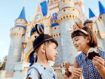 Magic Kingdom Park A young boy and girl eating ice cream sandwiches in front of Cinderella Castle