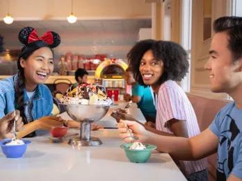 Disney Resort hotels Three adults laughing while sat at a table eating a large ice cream sundae