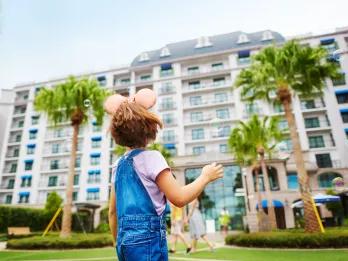 A young girl wearing Minnie Mouse ears looking up at a European-style hotel