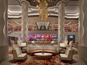 Coronado Springs - Gran Destino Tower The lobby of a hotel with clean white pillars and white chairs and booths surrounding small wooden tables and in the centre and beautiful circular shaped lights hanging down.