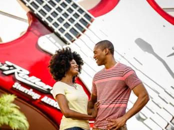 Couple stood in front of beige building with giant red guitar on the front with white strings and the name of the ride on the bottom left