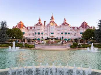 The exterior of a pink hotel behind a fountain and a flower bed in the shape of Mickey Mouse
