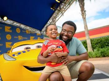 Lightning McQueen's Racing Academy A dad and young son posing in front of one of the cars from Pixar's Cars
