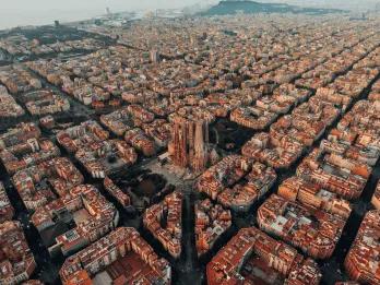 Barcelona Layout of Barcelona with a view of the Sagrada Familia cathedral. The city is laid out with straight roads and buildings shaped in squares. They all have the same colour scheme with white and orange walls and roofs.