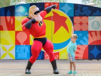 Disney's Hollywood Studios Character Meets A young boy posing with Mr Incredible in front of a gate painted with the Pixar Ball