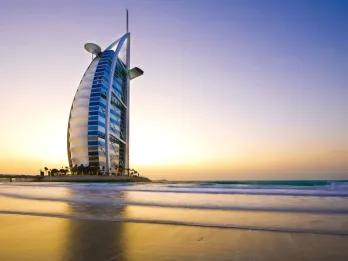 Burj Al Arab Sail shaped building coloured white with many windows and a helicopter pad on top. It is in the middle of the ocean on a man made island, with one road connecting it with mainland.