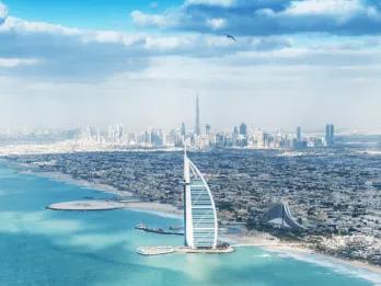 Dubai skyline View from over the crystal clear sea with a view of the beach with an island off of it with a sail shaped building on it called the Burj Al Arab. In the background you can see a view of the city skyline and the Burj Khalifa.