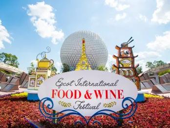 EPCOT International Food and Wine Festival White circular building shaped like a golf ball with a plant pot in front with a sign saying "Epcot International Food and Wine Festival" with cardboard cutouts of international recognisable structures such as the Eiffel Tower, built out of food.