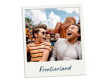 Frontierland Two kids, one boy wearing glasses and one girl, are sat on a ride with wild west theming. In the background there are large orange rocks.