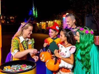Mickey’s Not-So-Scary Halloween Party A woman wearing a bat headband and a cast member nametag handing out sweets to guests who are dressed as Hei Hei, Moana and other Moana characters. The young boy is wearing a cap resembling a chicken and the girl is wearing a moana costumer and holding a plush of Pua the pig.
