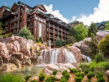 Large brown hotel with wooden detailing and approximately 6 floors surrounded by waterfalls and lush plants.