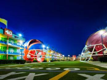 Large grass space with American football lines on the floor, each side there are buildings with large football helmet statues in front.