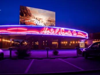 A neon sign reading Hotel Santa Fe underneath a large picture of Lightning McQueen and Sally from Cars