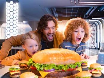A dad with his two children looking at a giant burger in shock